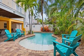 A pool area with a curved edge, surrounded by palm trees and a building with a yellow facade. - Holmes Beach - Pool - Minutes to Beach - Sleeps 8 (Holmes Beach)