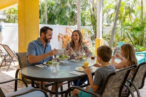 A family dining outdoors at a round table with chairs, surrounded by greenery. - Holmes Beach - Pool - Minutes to Beach - Sleeps 8 (Holmes Beach)