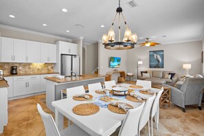 A modern kitchen with white cabinets, a central island, and a dining area with a table set for four. - Holmes Beach - Pool - Minutes to Beach - Sleeps 8 (Holmes Beach)