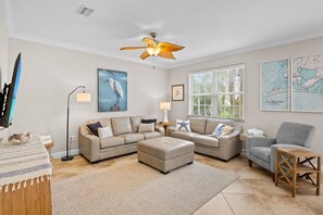 A spacious living room with a large sectional sofa, a smaller sofa, a coffee table, and a wooden side table. There is a floor lamp, a painting of a bird, and a map on the wall. - Holmes Beach - Pool - Minutes to Beach - Sleeps 8 (Holmes Beach)