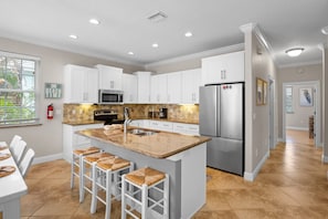 A modern kitchen with white cabinets, a stainless steel refrigerator, and a central island with bar stools. - Holmes Beach - Pool - Minutes to Beach - Sleeps 8 (Holmes Beach)