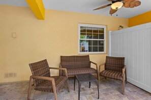 A room with three wicker chairs, a white door, and a window with a view of a house. - Holmes Beach - Pool - Minutes to Beach - Sleeps 8 (Holmes Beach)