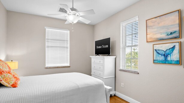 A bedroom with a bed, a ceiling fan, a TV, and two windows with blinds. - Holmes Beach - Pool - Minutes to Beach - Sleeps 8 (Holmes Beach)