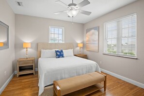 A bedroom with a bed, two bedside tables, a bench, a ceiling fan, and two windows with blinds. - Holmes Beach - Pool - Minutes to Beach - Sleeps 8 (Holmes Beach)