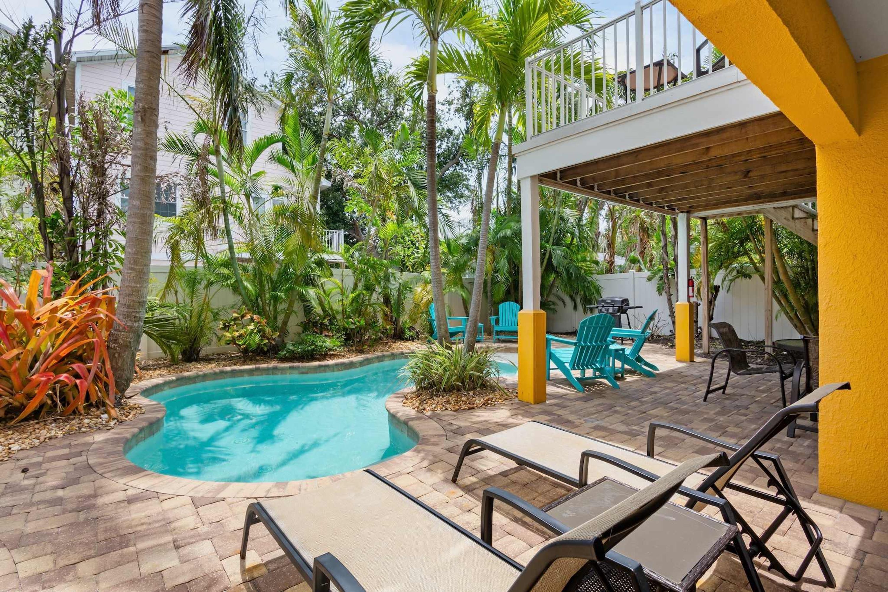 A pool area with lounge chairs, a covered seating area, and tropical vegetation.