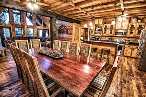 A wooden interior with a dining table surrounded by chairs, a kitchen area with wooden cabinets, and a large window providing natural light. - Stairway to Heaven 7BR Luxury Mountain Views (Broken Bow)