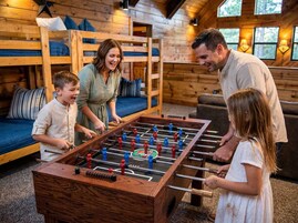 A family playing foosball in a cabin with wooden walls and a bunk bed.