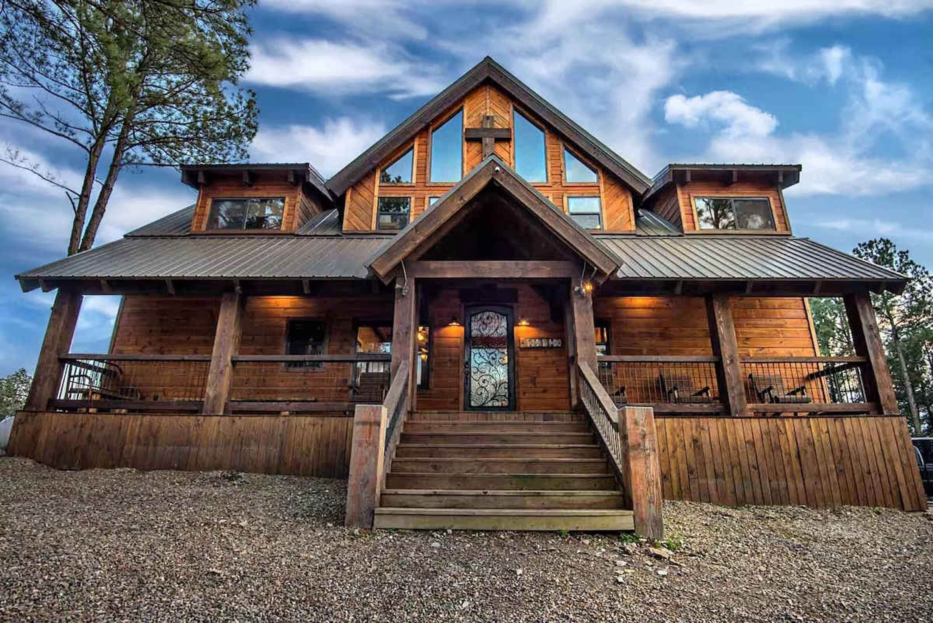 A wooden cabin with a steeply pitched roof, a front porch with steps, and a large window with decorative glass.