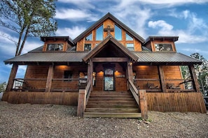 A wooden cabin with a steeply pitched roof, a front porch with steps, and a large window with decorative glass. - Stairway to Heaven 7BR Luxury Mountain Views (Broken Bow)