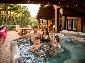 Una familia en un jacuzzi con una terraza de madera y mobiliario exterior.