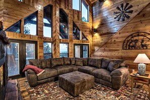 A spacious living room with a large sectional sofa, a patterned rug, and a wooden ceiling with skylights. - Stairway to Heaven 7BR Luxury Mountain Views (Broken Bow)