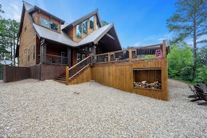 A wooden cabin with a sloped roof, a staircase leading to a deck, and a gravel driveway. - Stairway to Heaven 7BR Luxury Mountain Views (Broken Bow)