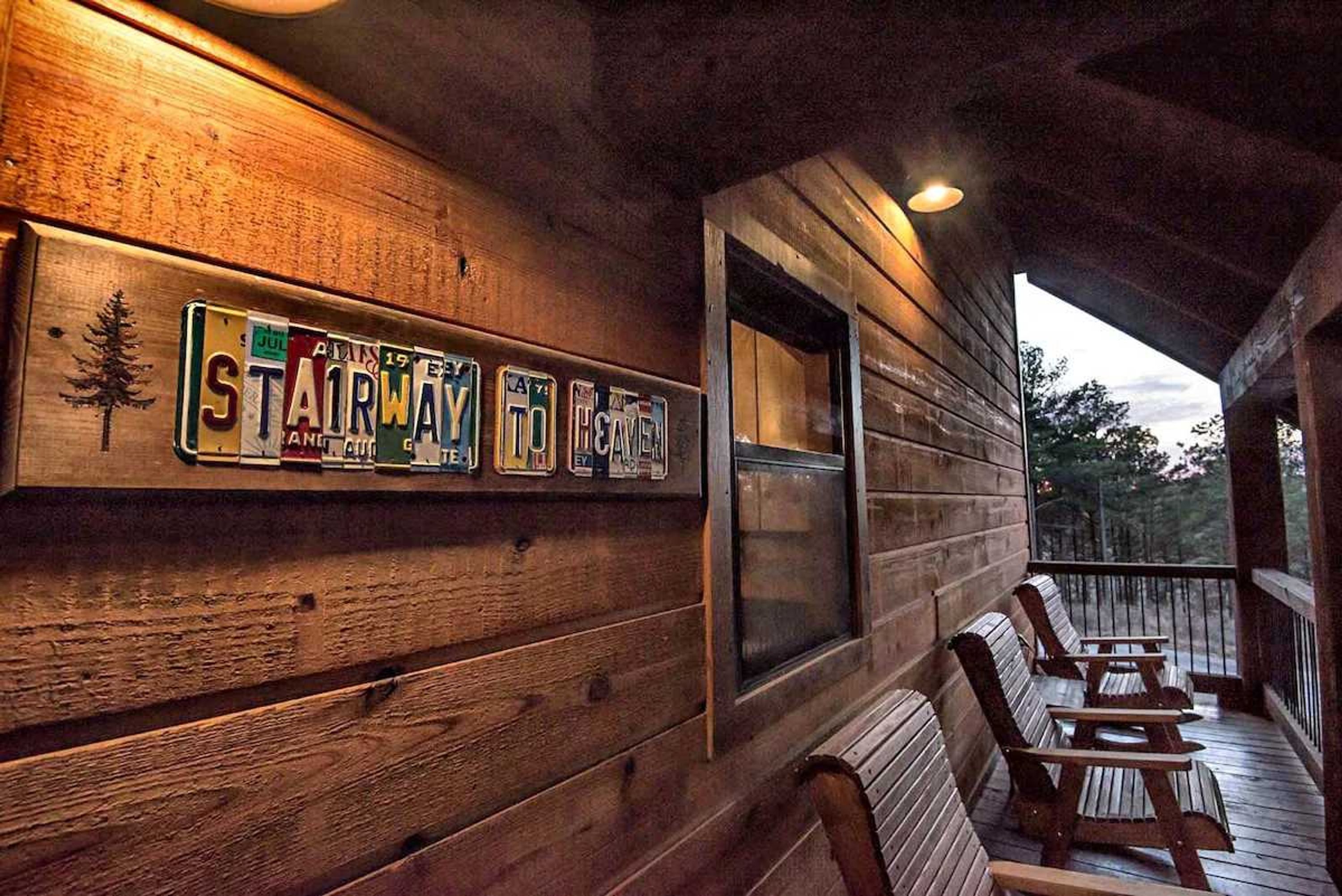 A wooden cabin with a porch, a row of license plates, and a view of the forest.