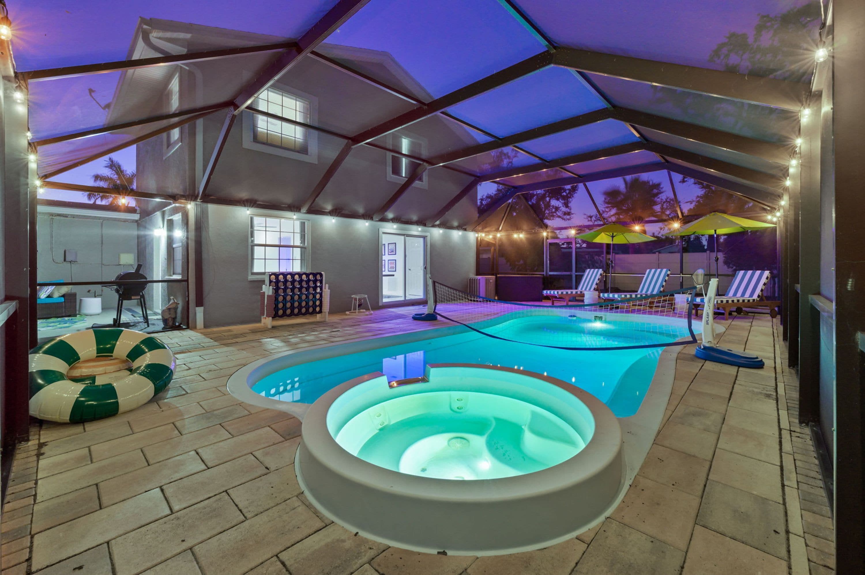 Ein Hallenbad mit Whirlpool, umgeben von Liegestühlen und Sonnenschirmen, unter einem überdachten Bereich mit Lichterketten.