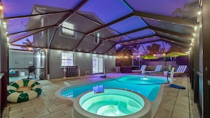 An indoor swimming pool with a hot tub, surrounded by lounge chairs and umbrellas, under a covered area with string lights. - Sleeps 16 Golf Simulator Pickleball Pool Spa (Bradenton)