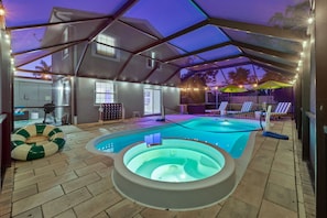 Ein Hallenbad mit Whirlpool, umgeben von Liegestühlen und Sonnenschirmen, unter einem überdachten Bereich mit Lichterketten.