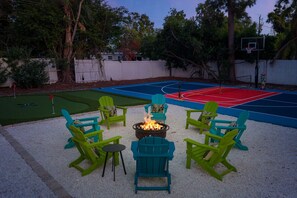 Ein Garten mit Basketballfeld, Feuerstelle und grünen Adirondack-Stühlen.