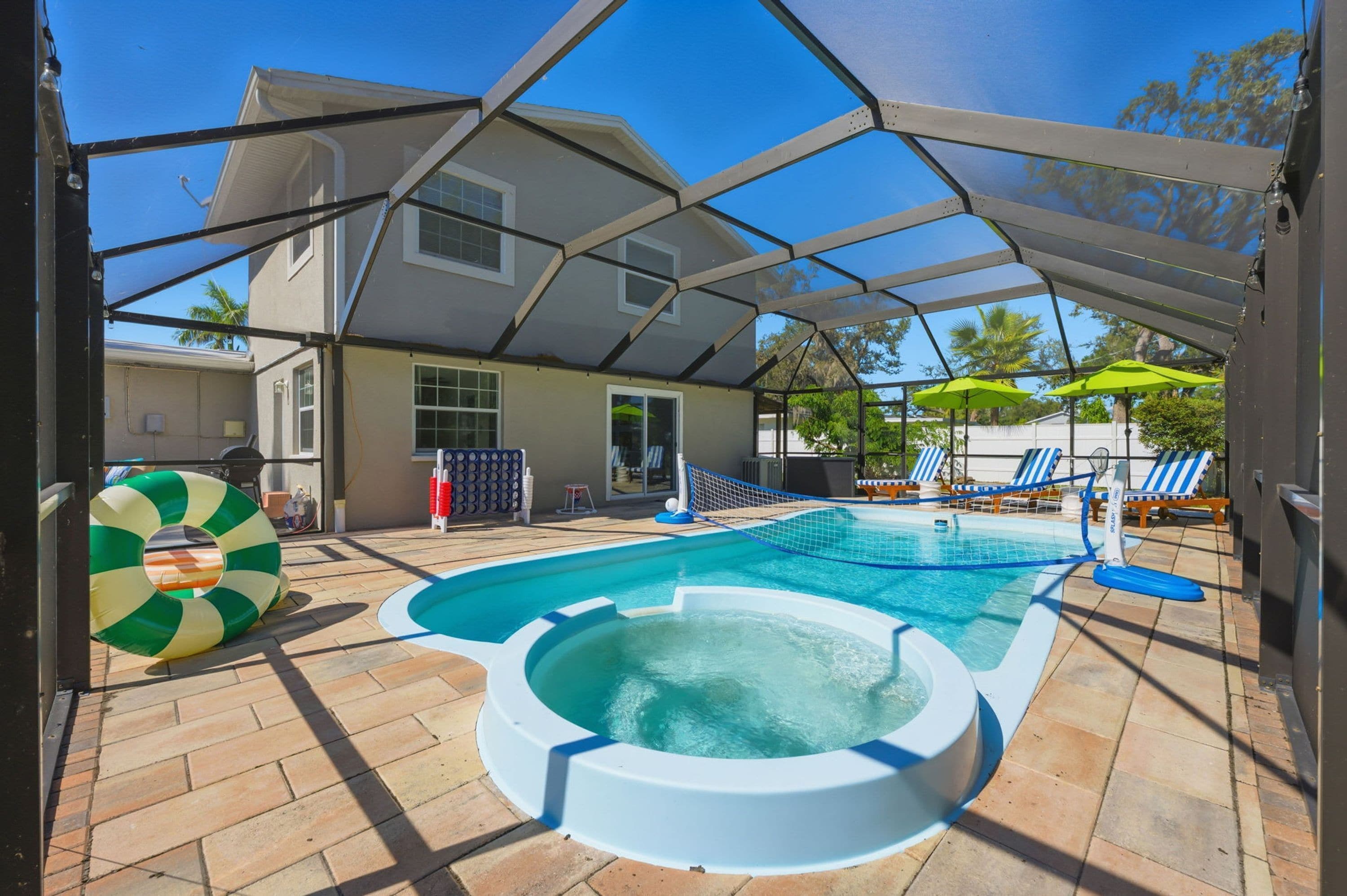 A covered swimming pool with a hot tub, lounge chairs, and umbrellas.