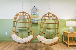 Two wicker hanging chairs with cushions, a small shelf with children's books, and a bedside table with a lamp. - Manatee Haven Pool Games Hot Tub Firepit (Bradenton)