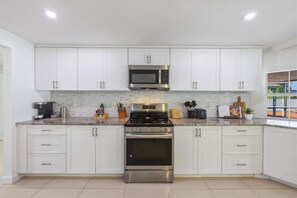 A modern kitchen with white cabinets, stainless steel appliances, and a tiled backsplash. - Manatee Haven Pool Games Hot Tub Firepit (Bradenton)