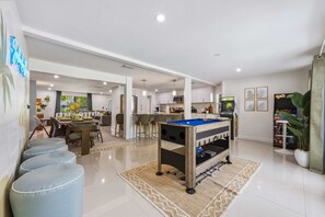 A modern living room with a pool table, a dining area with a sofa and chairs, and a kitchen in the background. - Manatee Haven Pool Games Hot Tub Firepit (Bradenton)