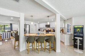 A modern kitchen with a central island, bar stools, and a retro gaming console. - Manatee Haven Pool Games Hot Tub Firepit (Bradenton)