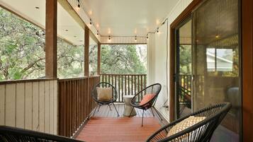 A covered porch with two chairs and a table, wooden railings, and a view of trees.