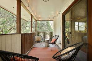 A covered porch with two chairs and a table, wooden railings, and a view of trees. - Poolside Pickleball Heated Pool Sleeps 20 (San Antonio)