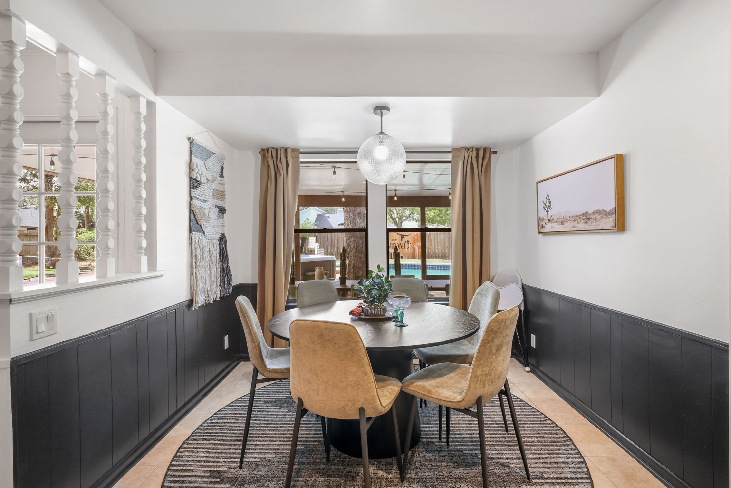 A dining area with a round table, six chairs, a chandelier, and a view of the outdoors.