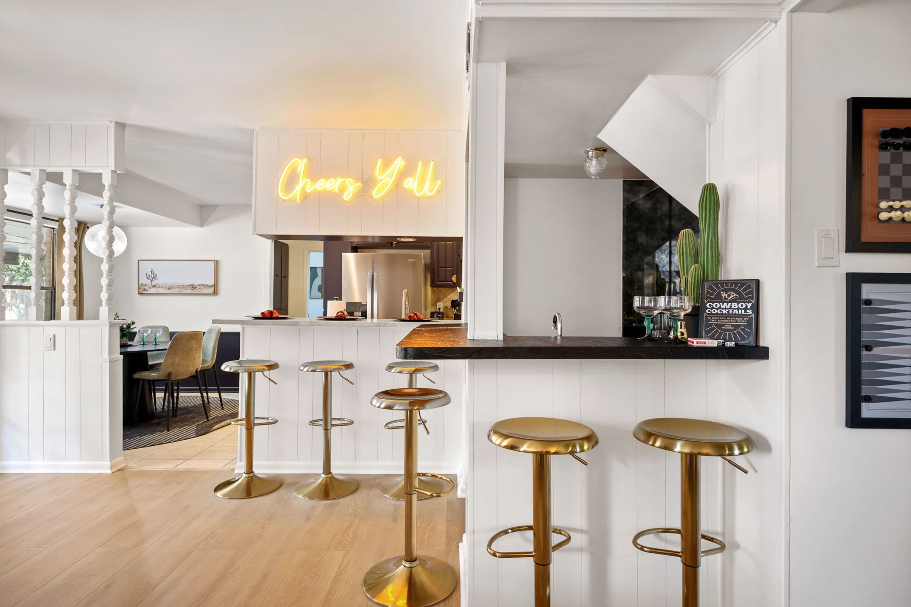 A modern kitchen with a neon sign, a bar area with stools, and a dining space with chairs.