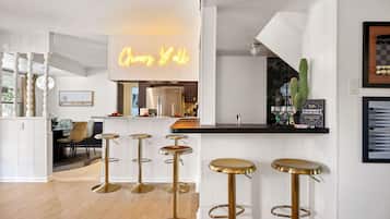 A modern kitchen with a neon sign, a bar area with stools, and a dining space with chairs.