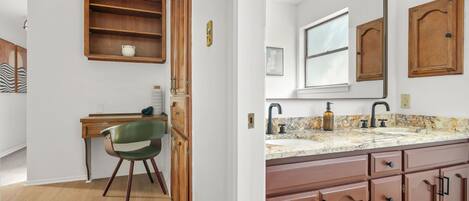 A room with a wooden desk, a chair, a wooden cabinet, a mirror, a sink, and a window.