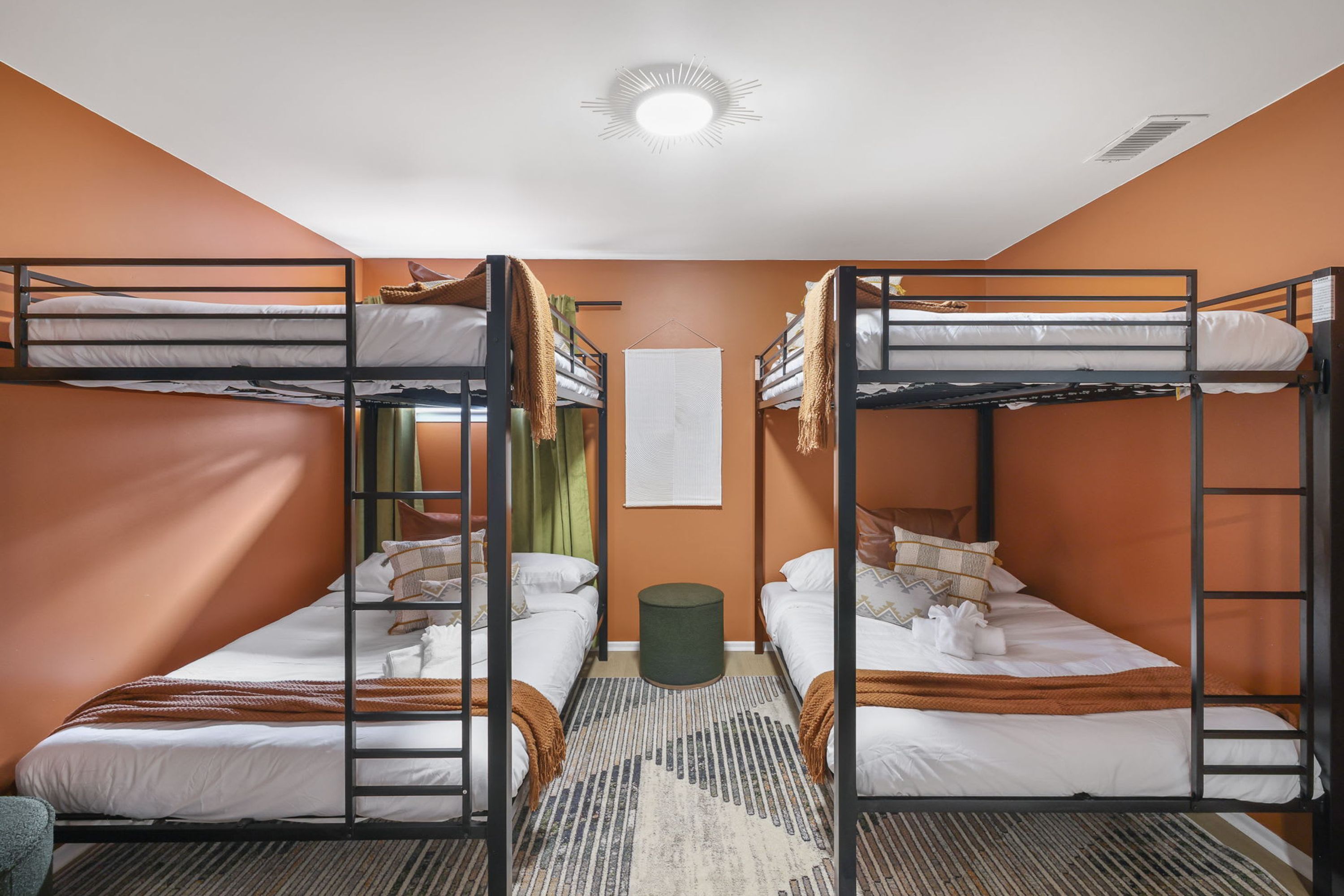Une chambre de dortoir avec des lits superposés, un petit tapis et un luminaire fixé au mur.