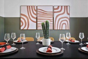Ein Esstisch, gedeckt für sechs Personen, mit einem Kaktus als Mittelpunkt, umgeben von Stühlen, und eine Wand mit abstrakter Kunst.