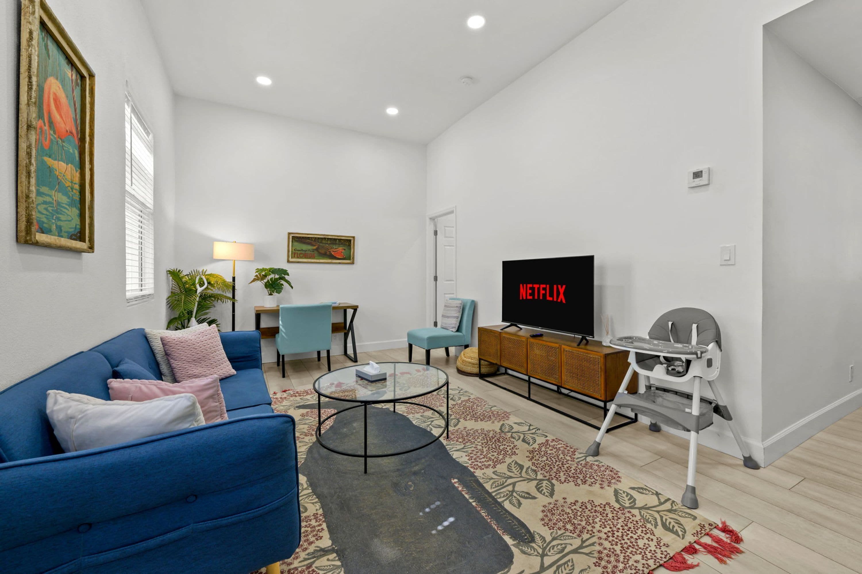 A living room with a blue sofa, a glass coffee table, a TV, and a high chair.