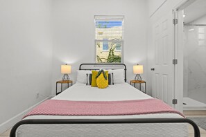 A bedroom with a bed, two bedside tables with lamps, a window with blinds, and a door leading to a bathroom. - Pineapple Paradise - 13 min to Beach - Fire Pit (Sarasota)