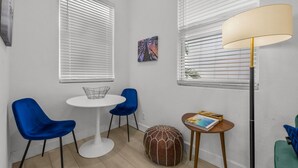 A room with two white round tables, one with a wire basket and one with a book. There are two blue chairs, a brown ottoman, and a floor lamp. - Pineapple Paradise - 13 min to Beach - Fire Pit (Sarasota)