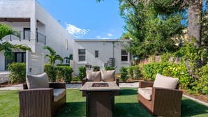 A patio area with wicker furniture and a table, surrounded by well-maintained grass and plants. - Pineapple Paradise - 13 min to Beach - Fire Pit (Sarasota)