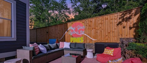 An outdoor seating area with a wooden fence, a colorful sign, and a variety of seating options including a red bean bag.