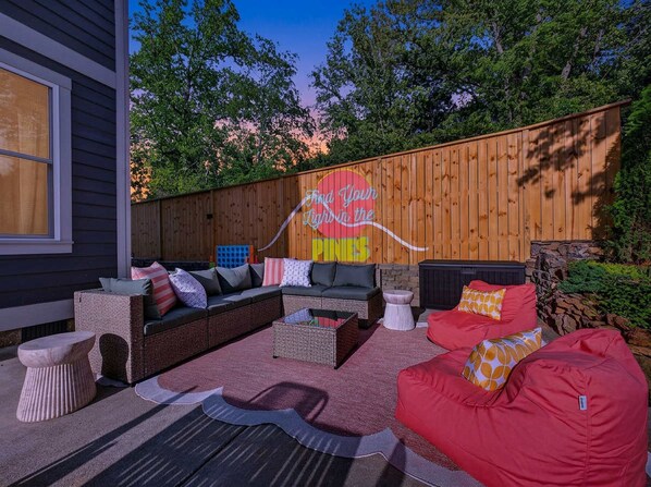 An outdoor seating area with a wooden fence, a colorful sign, and a variety of seating options including a red bean bag. - Outdoor Games Hot Tub Firepit Grill Sauna (Asheville)