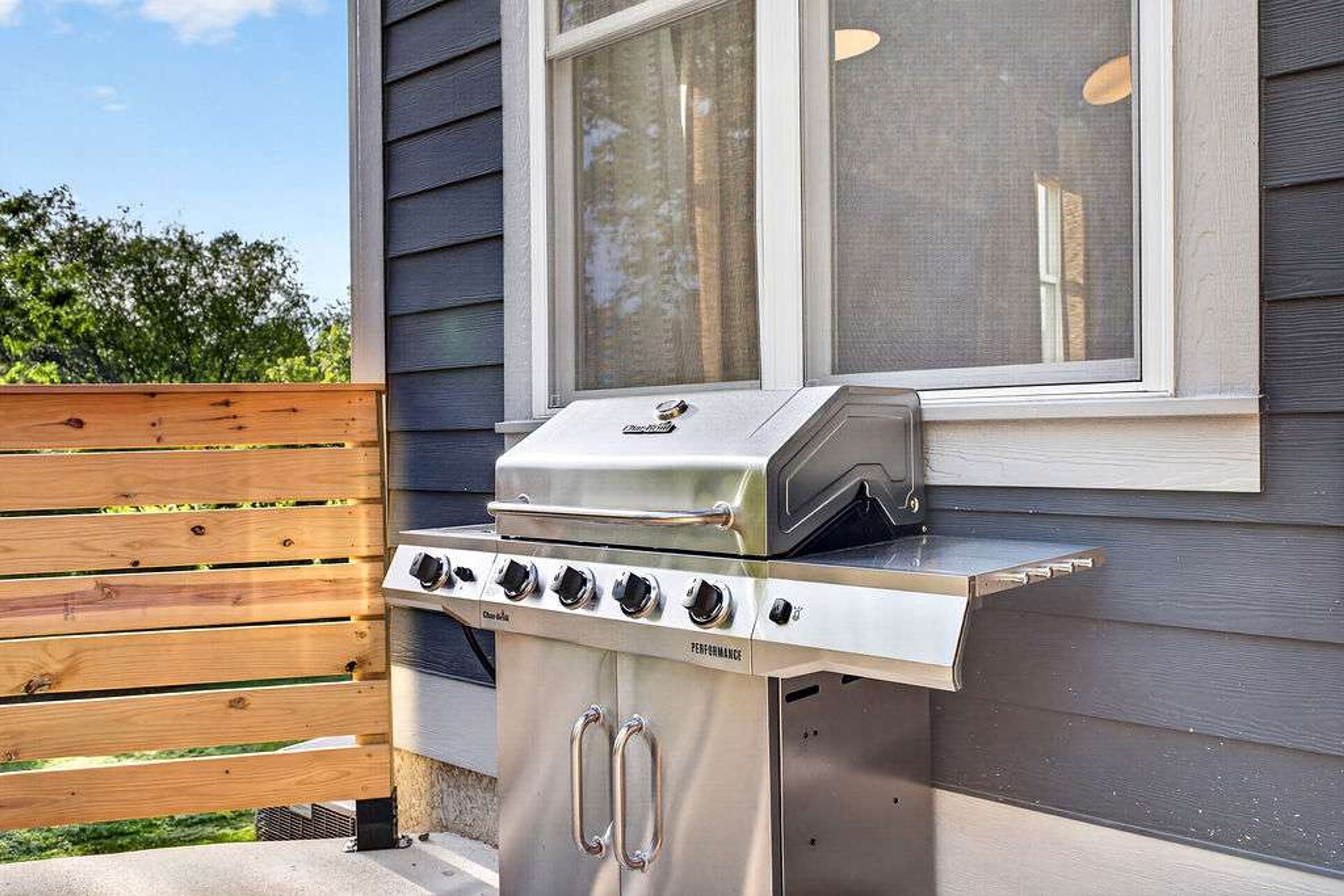 Ein Grill für den Außenbereich mit Bedienfeld und Schornstein, vor einem Haus mit Fenster und Holzzaun platziert.