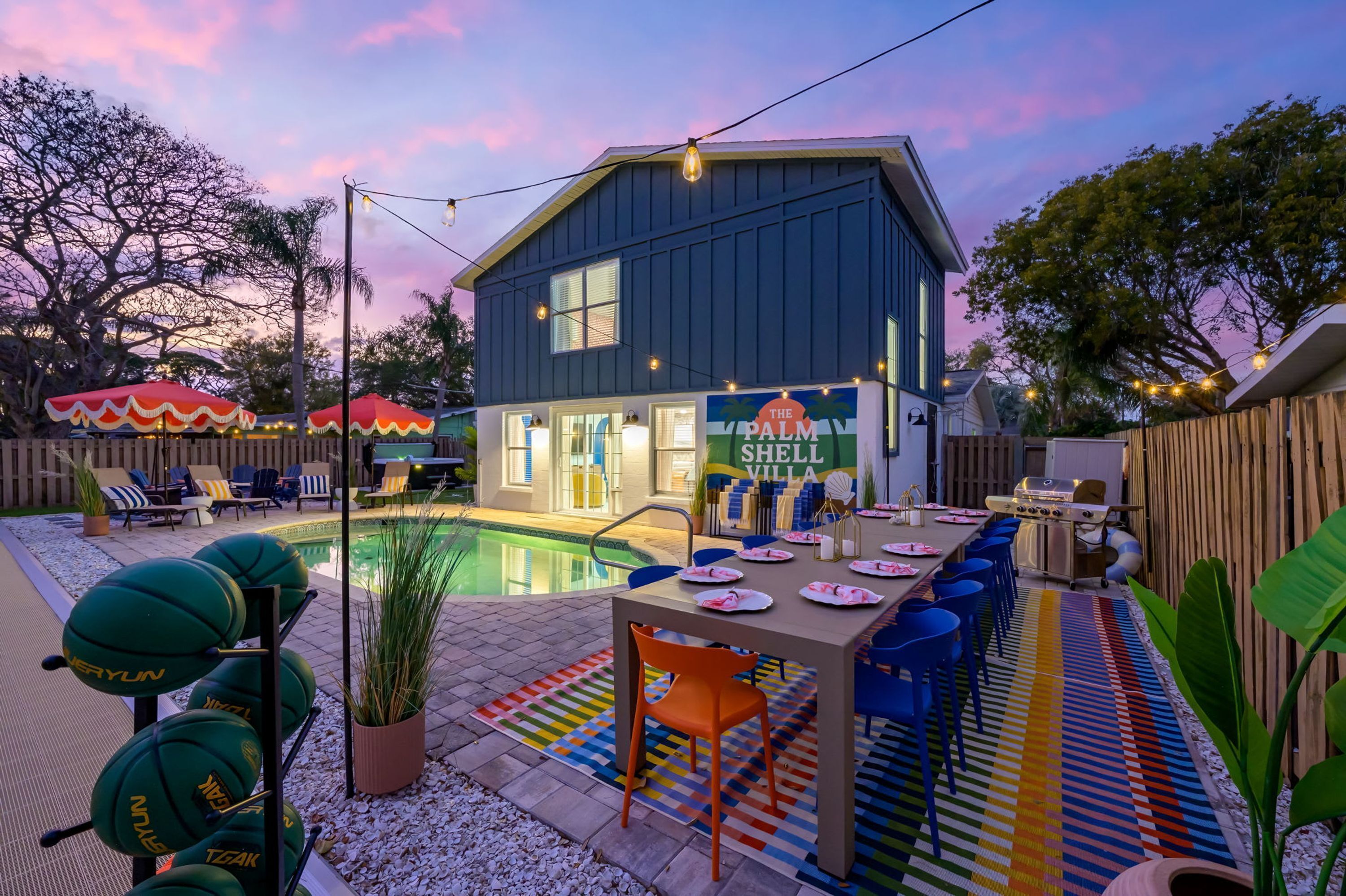 A poolside area with a dining setup, a sign for 'The Palm Shell Villa,' and outdoor seating with umbrellas.