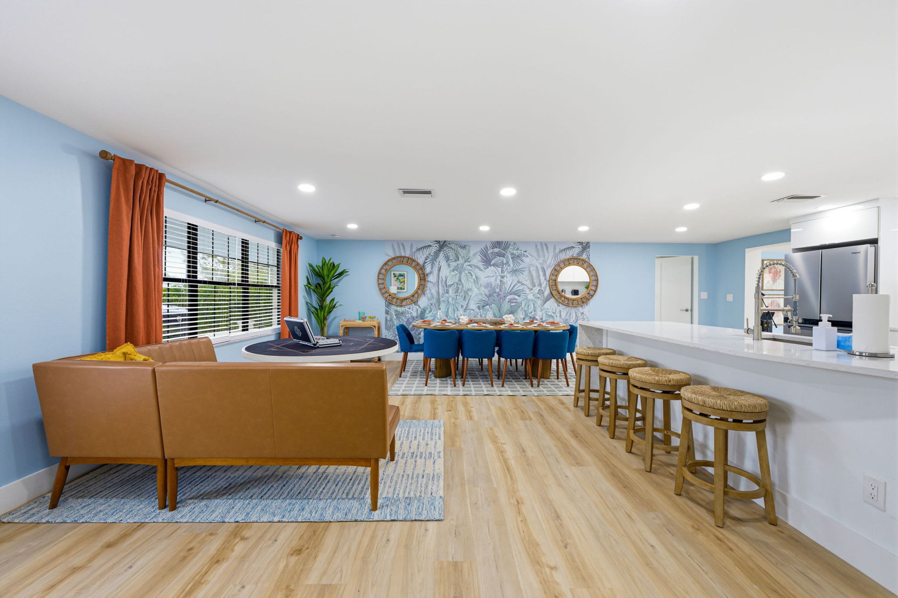 Une cuisine moderne avec un îlot central, un coin repas avec des chaises bleues et un espace de vie avec un canapé marron.