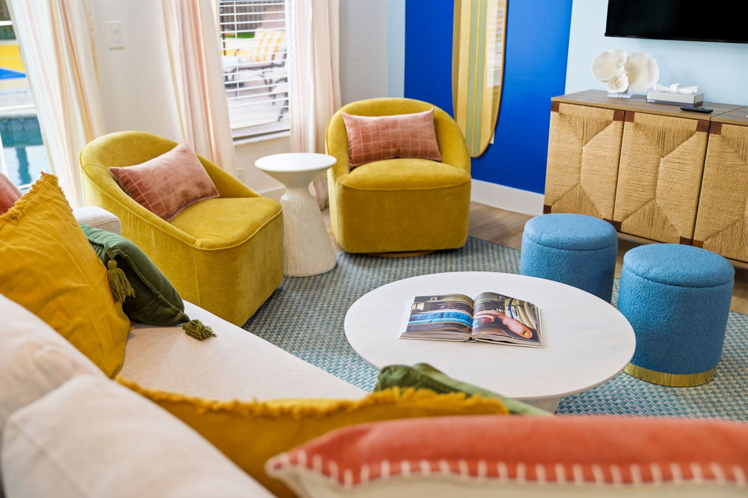 A modern living room with yellow armchairs, a white coffee table, and a blue ottoman.