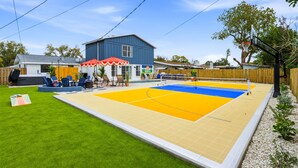 Een achtertuin met een volleybalveld, een barbecueplek en een gebouw met een blauwe gevel.