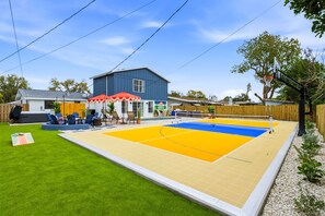 A backyard with a volleyball court, a barbecue area, and a building with a blue exterior. - Palm Shell Villa - Pool - Pickleball - Hot Tub (Bradenton)