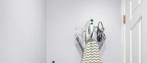 A room with a wooden floor, a blue vacuum cleaner, and an iron on a stand.