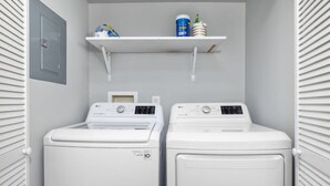 Uma área de lavanderia com duas máquinas de lavar de carregamento frontal brancas e uma prateleira acima delas.