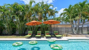A swimming pool with lounge chairs and umbrellas, surrounded by palm trees. - Sleeps 10 Pool Slide Pickleball Fire Pit (Seminole)