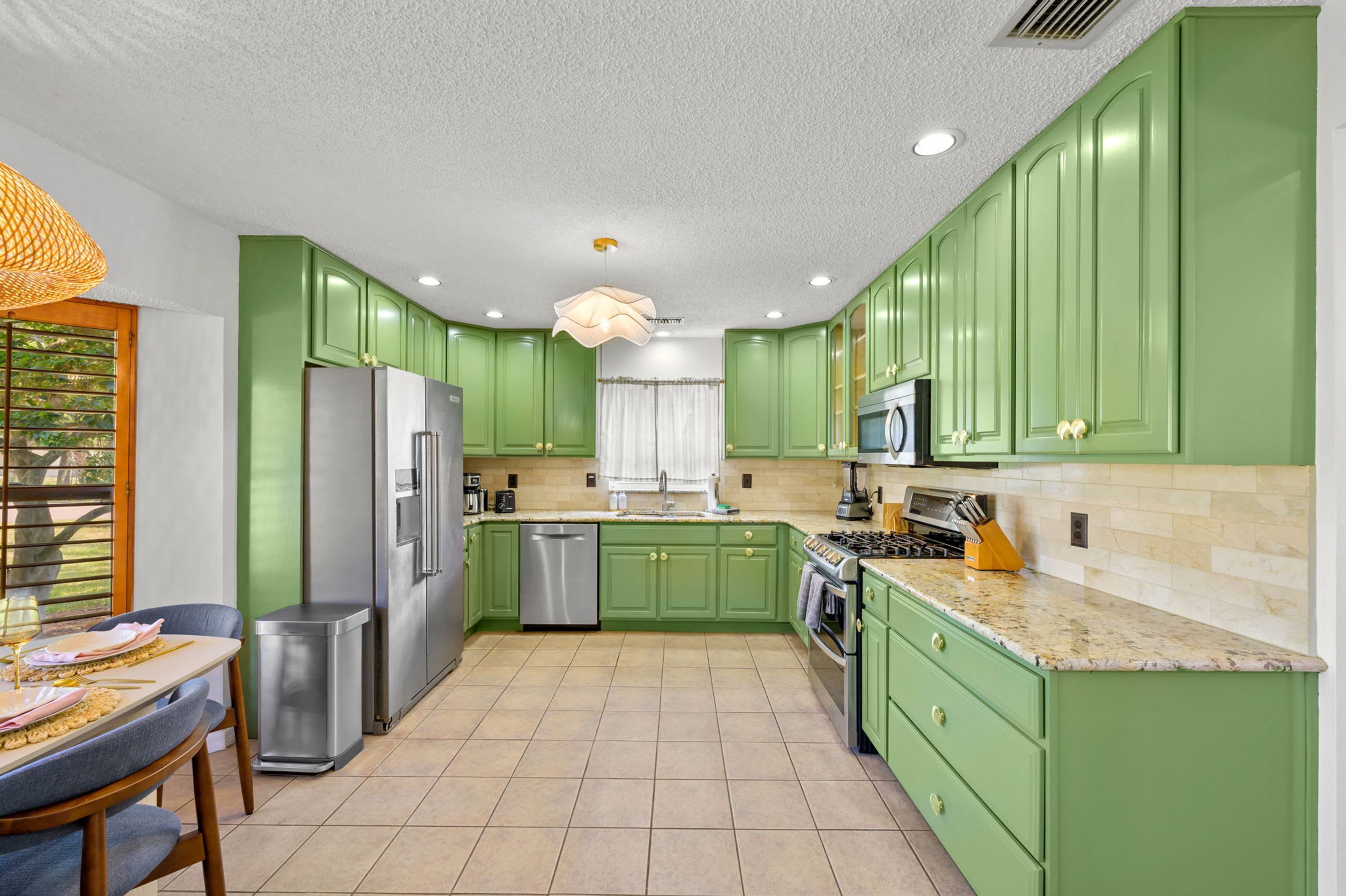 Una cocina con armarios verdes, electrodomésticos de acero inoxidable y piso de baldosas.